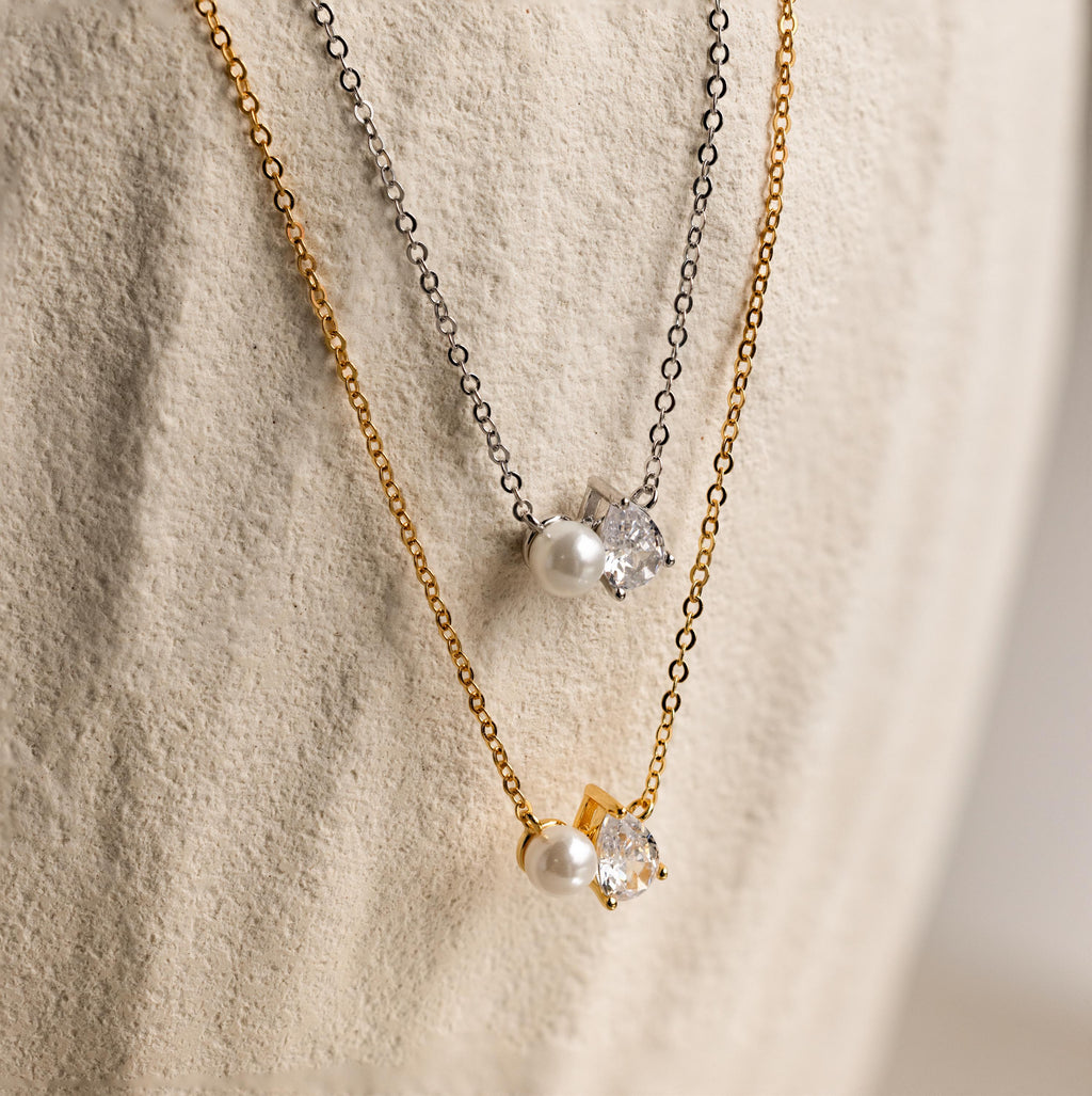 Two Pearl Diamond Necklaces with pearl and teardrop diamond pendants on gold and silver chains, displayed on a textured surface.