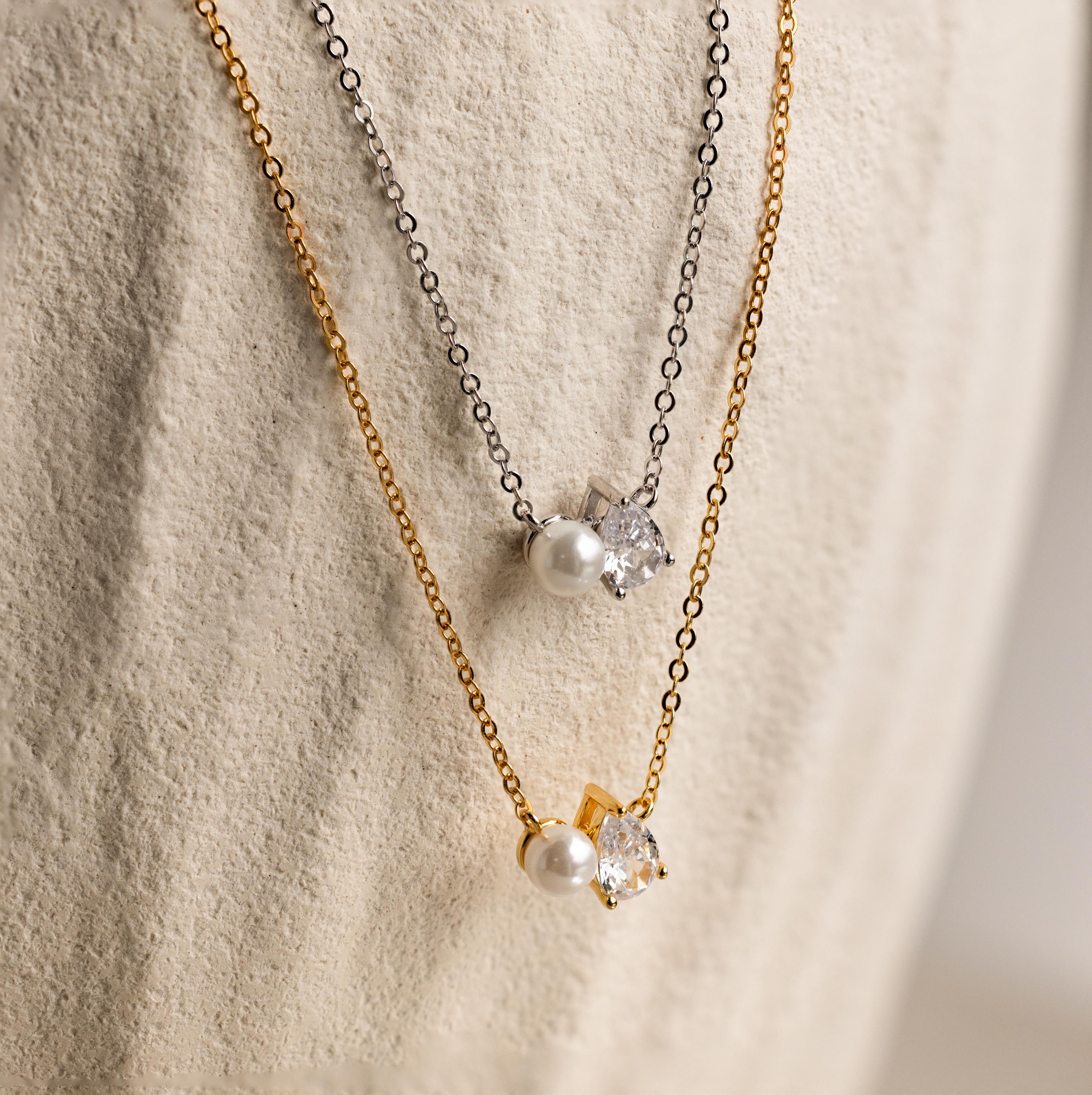 Two Pearl Diamond Necklaces with pearl and teardrop diamond pendants on gold and silver chains, displayed on a textured surface.
