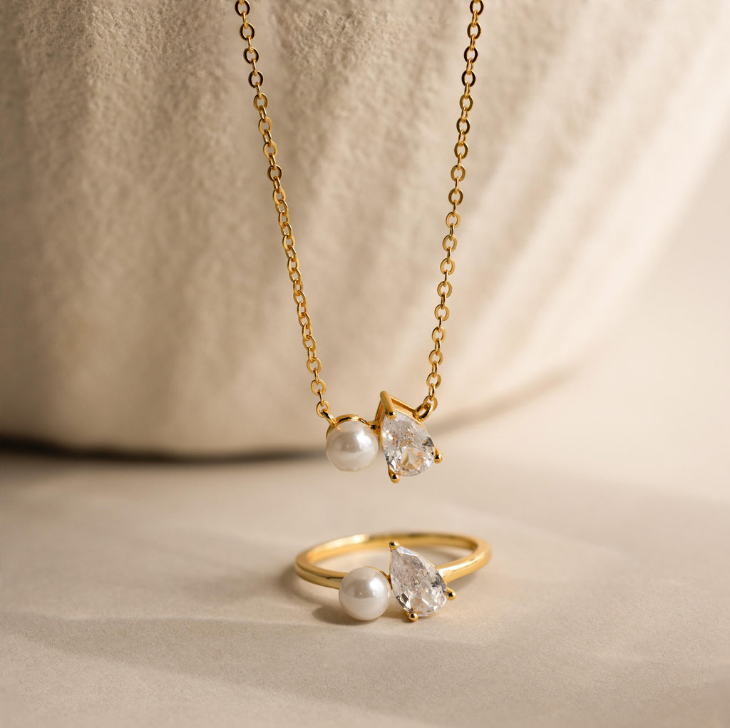The Pearl Diamond Necklace features pearl accents and a teardrop diamond, elegantly showcased on a neutral background.