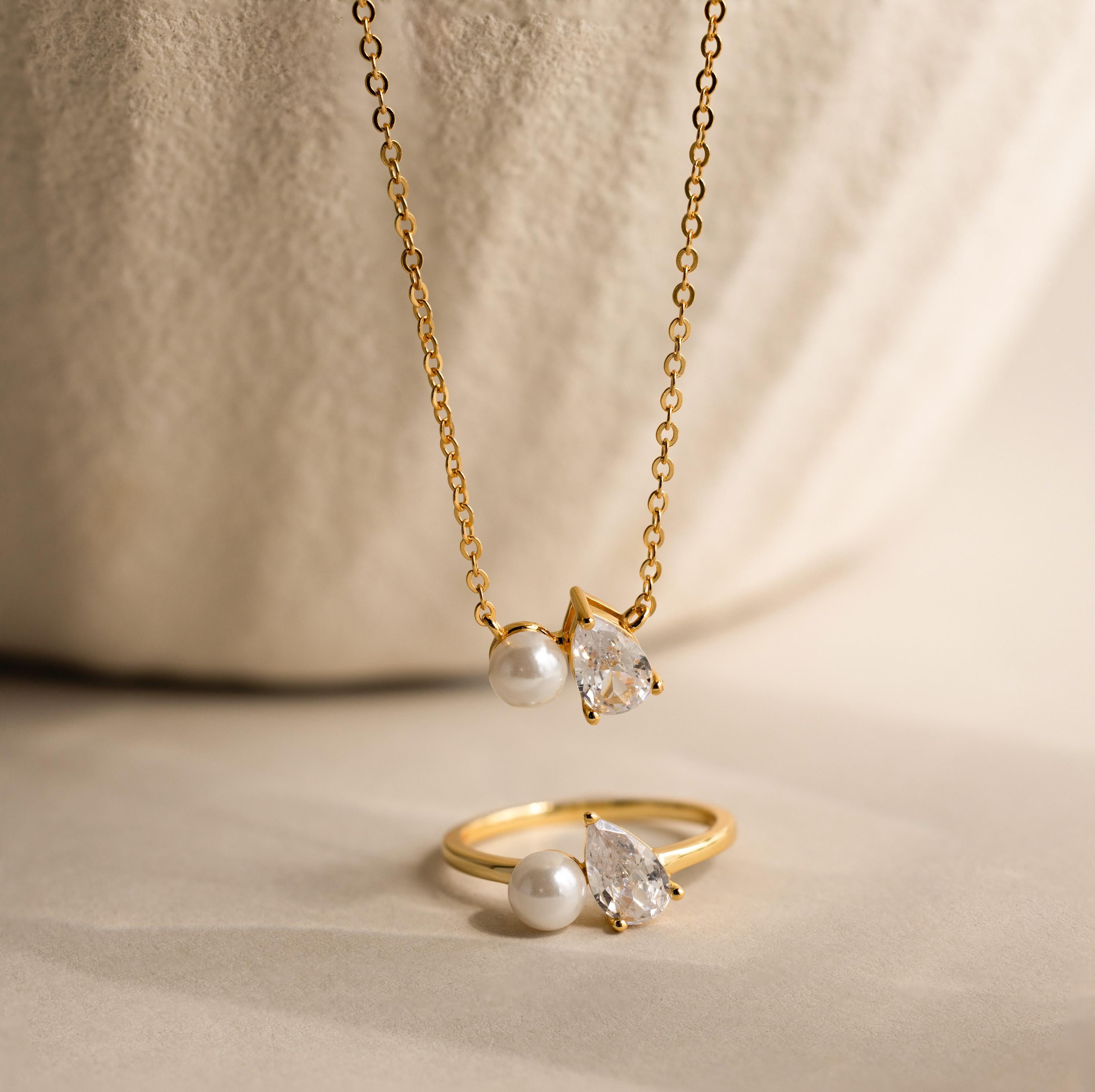 The Pearl Diamond Necklace features pearl accents and a teardrop diamond, elegantly showcased on a neutral background.