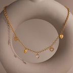Gold heart charm necklace displayed on a sculptural prop, featuring five heart-shaped pendants.