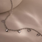 Silver heart charm necklace with five unique heart pendants displayed on a soft beige background.