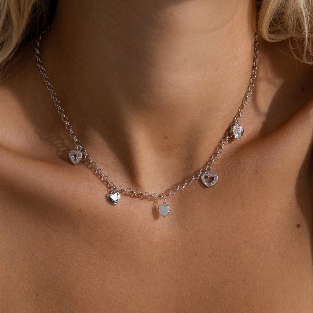 Model wearing a silver heart charm necklace featuring five unique heart pendants.