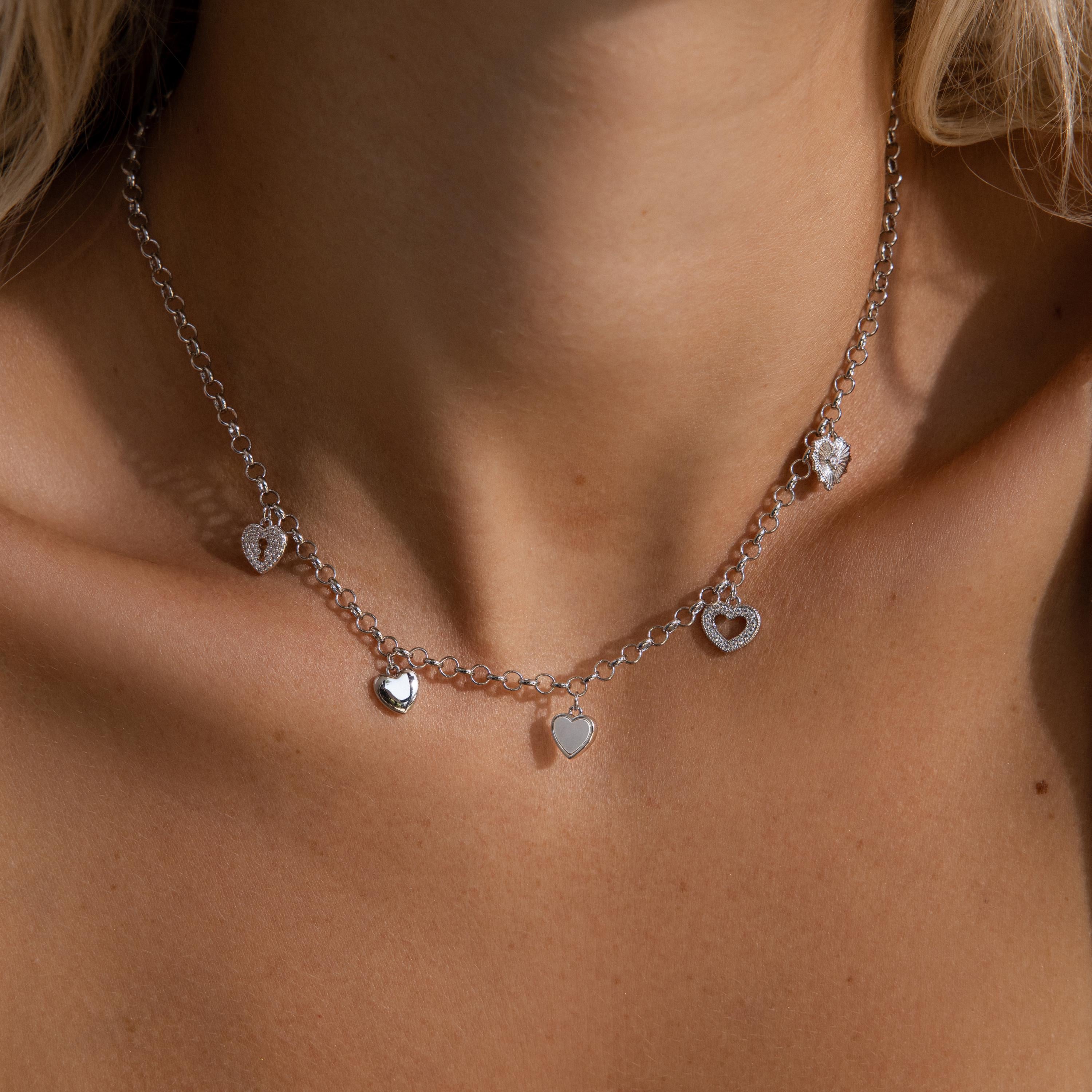 Model wearing a silver heart charm necklace featuring five unique heart pendants.