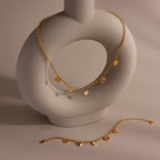 Gold heart charm necklace and matching bracelet displayed on a ceramic sculpture, featuring multi-style heart pendants and chunky rolo chain.