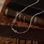 The Love Knot Chain Necklace in White Gold with a silver chain is displayed on two vintage books with ornate covers, symbolizing meaningful bonds.