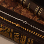 The Love Knot Chain Necklace rests elegantly on the spines of antique, ornate books, its delicate design adding a touch of timeless charm.