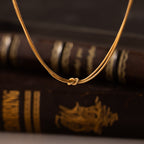 The Love Knot Chain Necklace in 18K Gold rests before vintage dark-bound books with gold accents, symbolizing meaningful bonds.