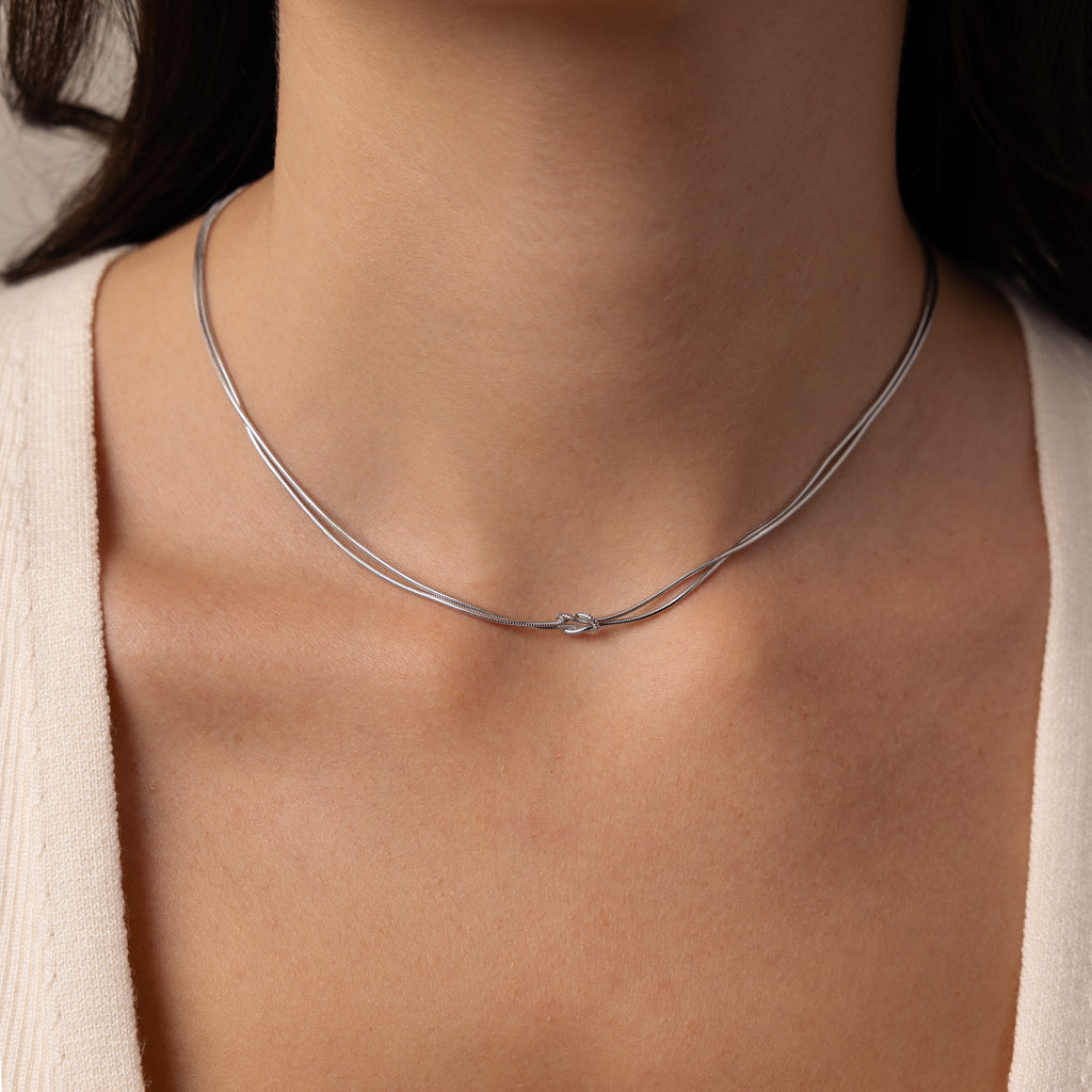 A close-up of a woman wearing the Love Knot Chain Necklace in White Gold, featuring a delicate knot detail that symbolizes meaningful bonds.