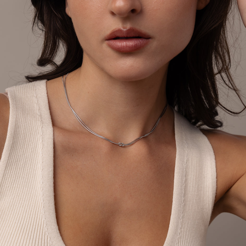 Woman wearing a cream sleeveless top and the Love Knot Chain Necklace in White Gold, shown from shoulders to chin.