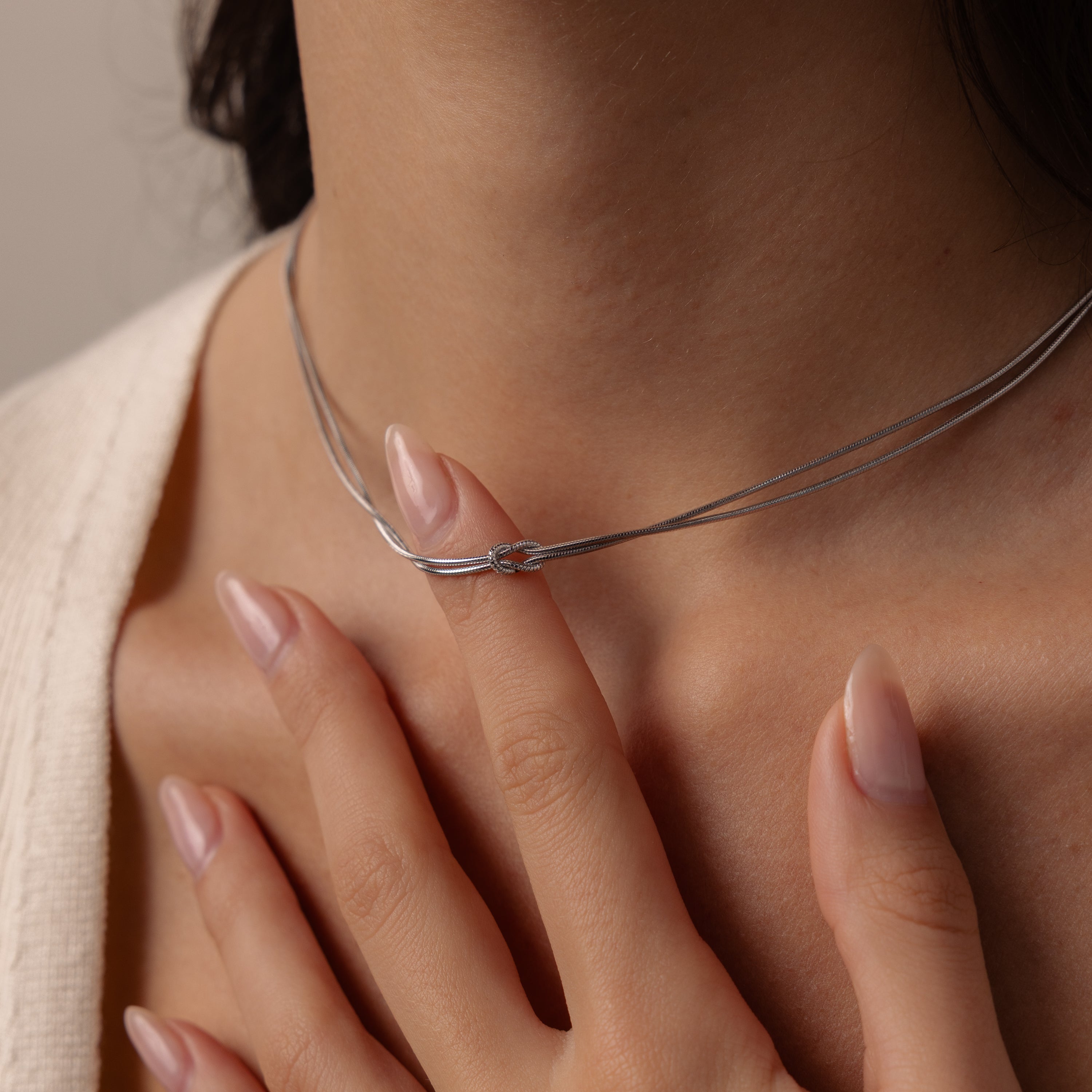 A close-up of a woman wearing the Love Knot Chain Necklace in White Gold, gently touching her collarbone with manicured fingers—a subtle nod to meaningful bonds.