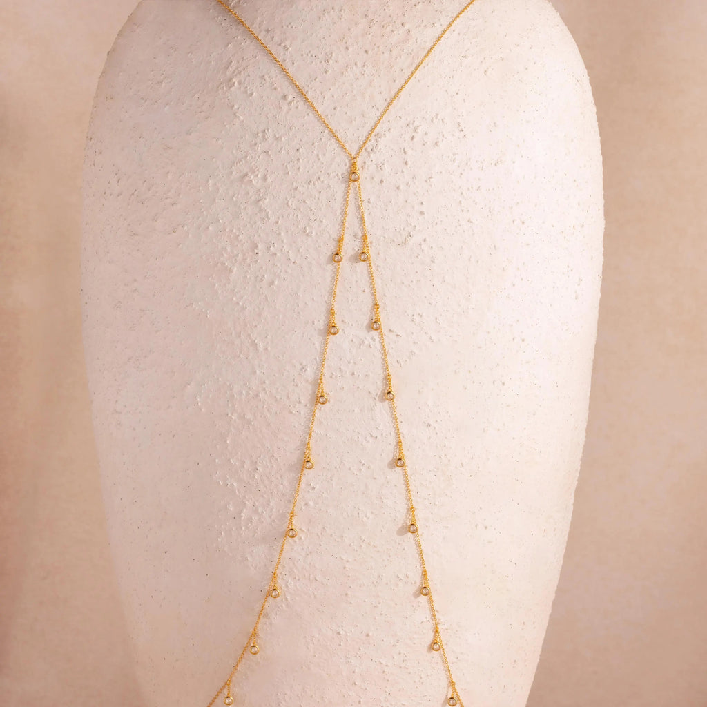 Full view of the 18k gold Diamond Station Body Chain displayed on a textured neutral-toned bust, showcasing its Y-shape silhouette and evenly spaced diamonds