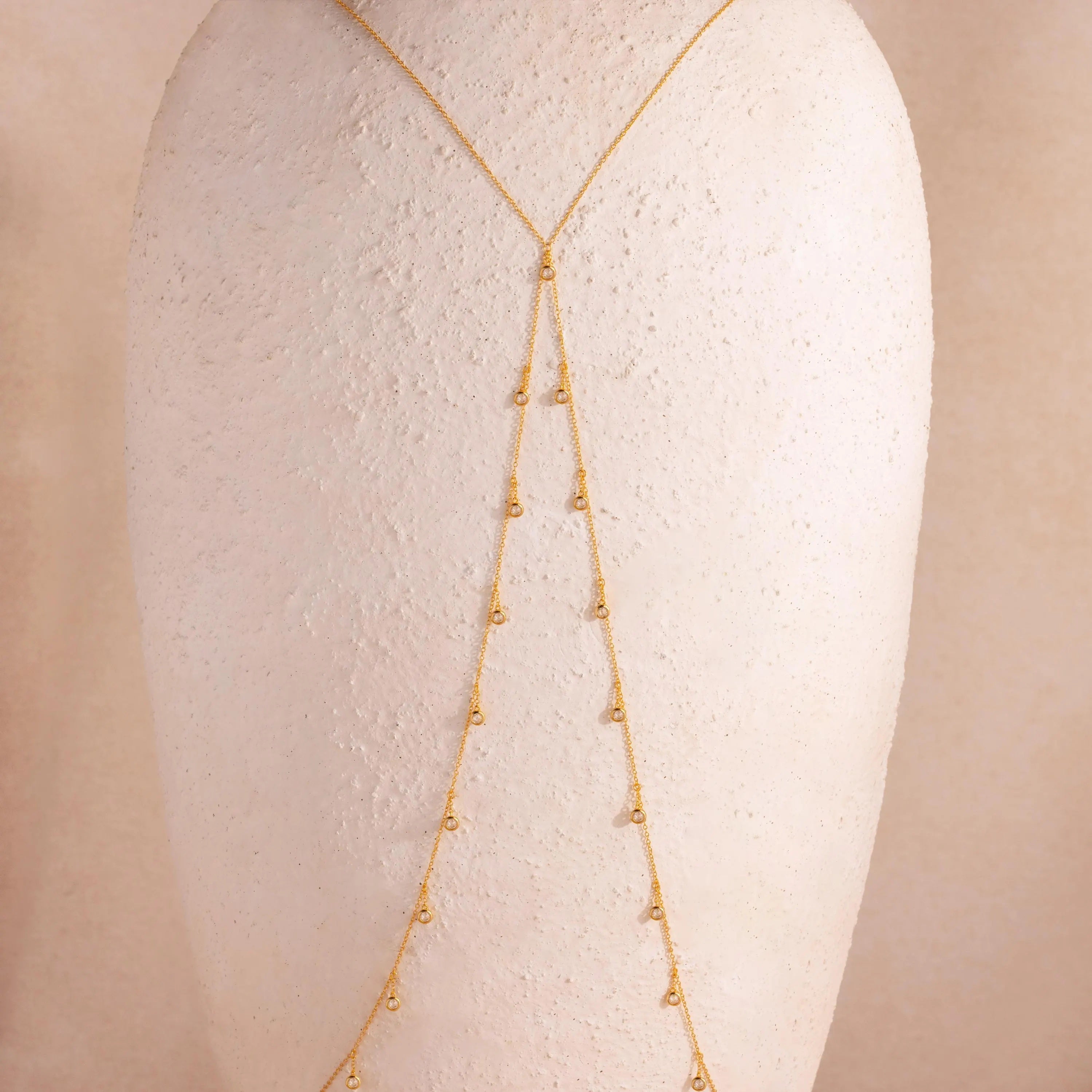 Full view of the 18k gold Diamond Station Body Chain displayed on a textured neutral-toned bust, showcasing its Y-shape silhouette and evenly spaced diamonds