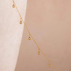 18k gold chain with round bezel-set diamond  crystals spaced delicately along its length against a soft neutral background.