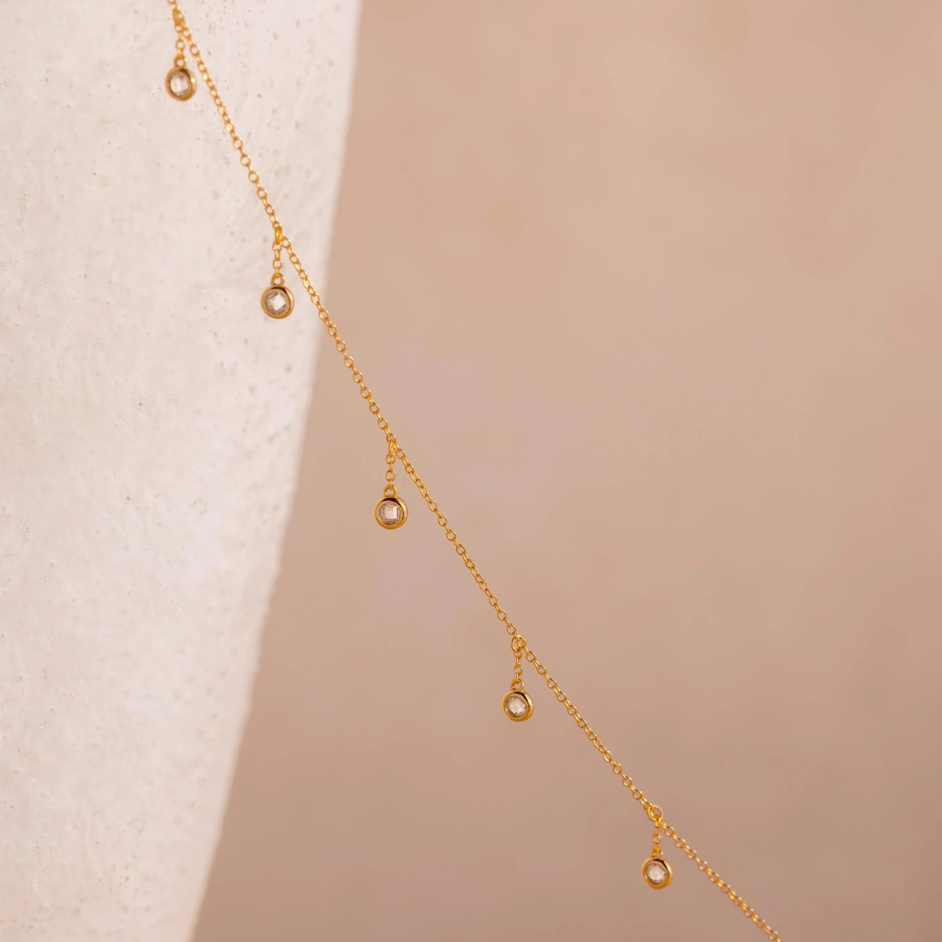 18k gold chain with round bezel-set diamond  crystals spaced delicately along its length against a soft neutral background.
