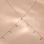 Close-up of the sterling silver Diamond Station Body Chain laid out in an X-shape on a soft blush satin backdrop.