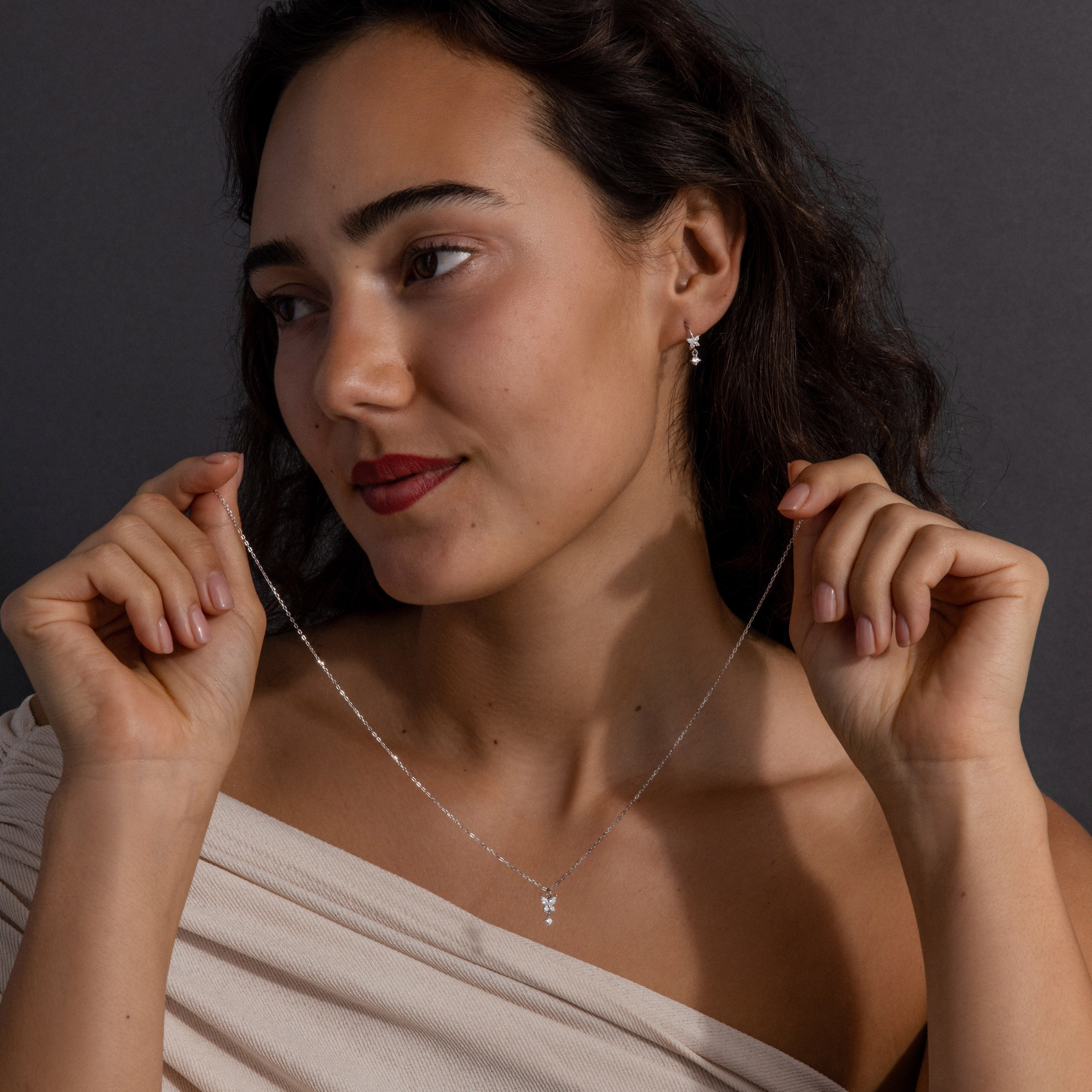 A woman in an off-shoulder top showcases the Diamond Butterfly Drop Jewelry Set—featuring a delicate butterfly necklace and matching huggie earrings—against a dark background.