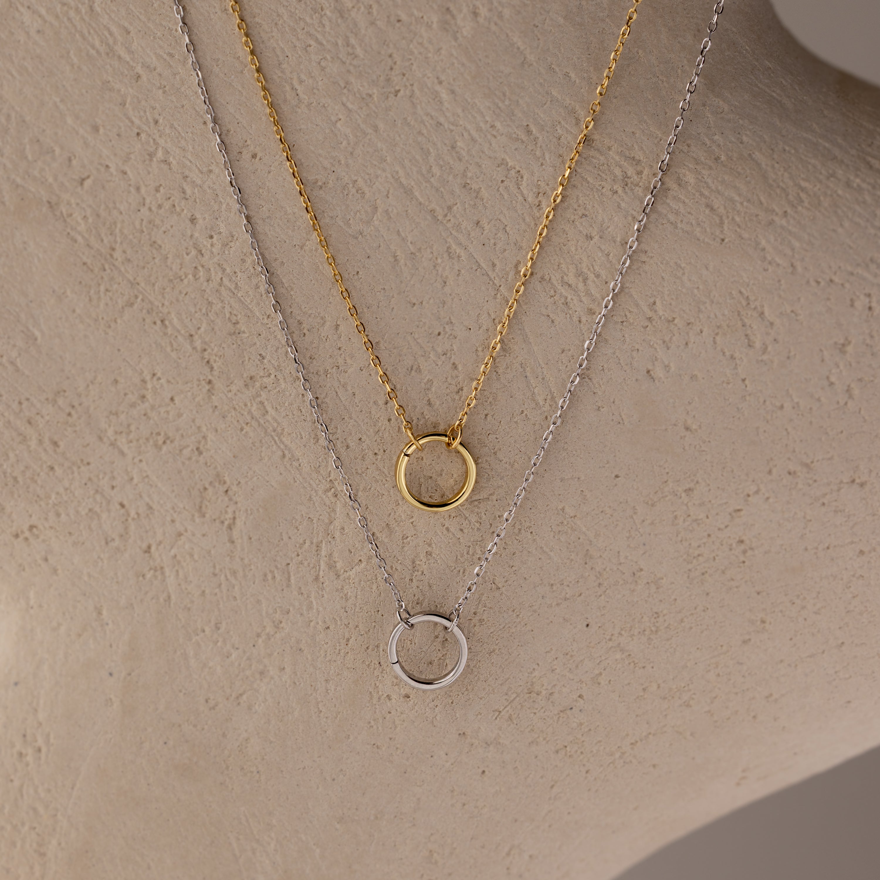 The Large Rolo Clasp Necklace, shown in gold and silver on a beige surface, is a modern must-have that’s perfect for layering with your favorite statement chain.