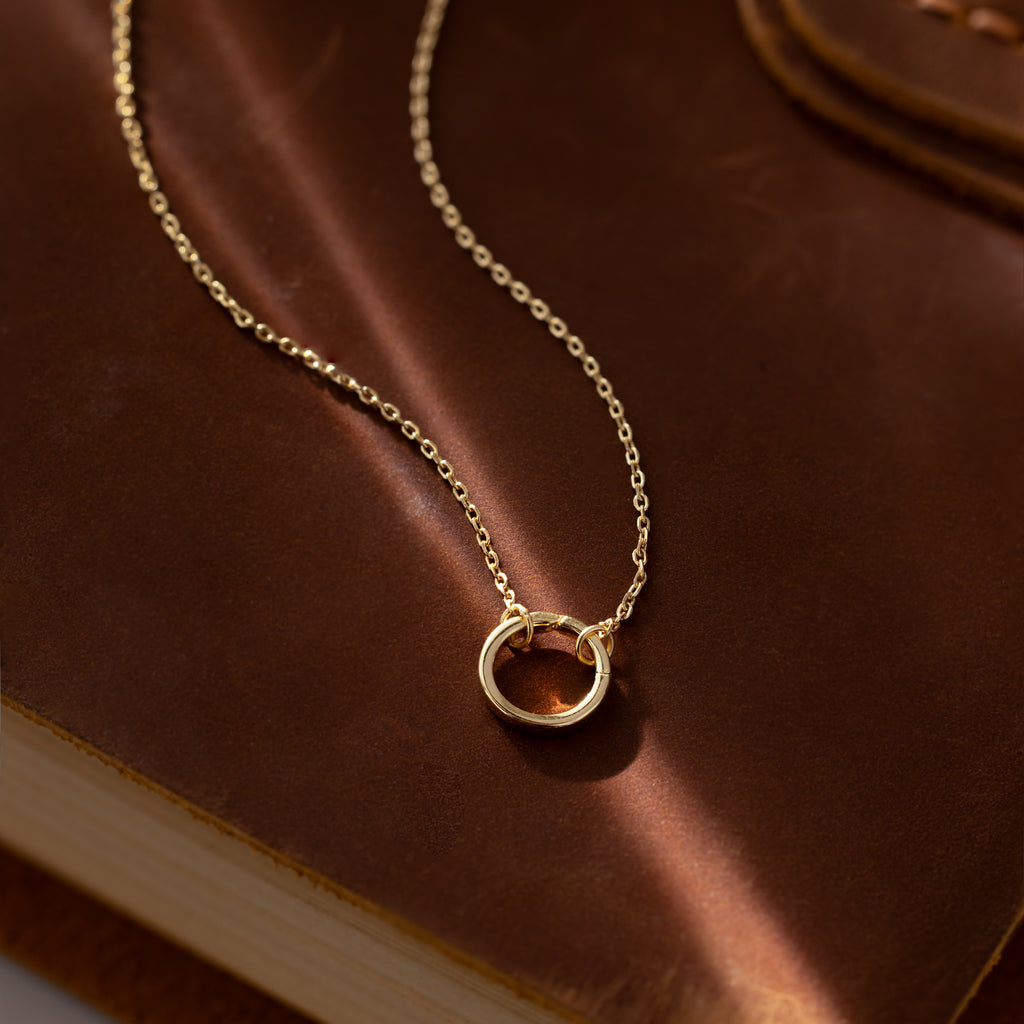 The Large Rolo Clasp Necklace in 18K Gold features a striking gold circle pendant on a statement chain, elegantly displayed on a brown leather-bound book.