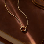 The Large Rolo Clasp Necklace in 18K Gold features a striking gold circle pendant on a statement chain, elegantly displayed on a brown leather-bound book.