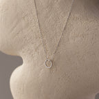 The Large Rolo Clasp Necklace in Sterling Silver features a delicate circle pendant, displayed on a textured beige mannequin—a versatile piece for effortless elegance.