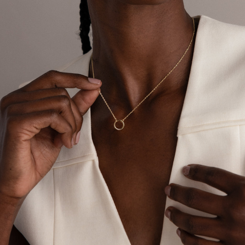 A person wearing a cream blazer holds the Large Rolo Clasp Necklace in 18K Gold, featuring a bold chain and an elegant clasp accent.