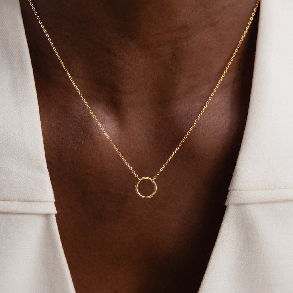 Close-up of the Large Rolo Clasp Necklace in 18K Gold, featuring a simple circle pendant, styled for layering and paired with a white blazer.