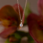 Close up of our Opal Diamond Necklace in Sterling Silver, against a floral background