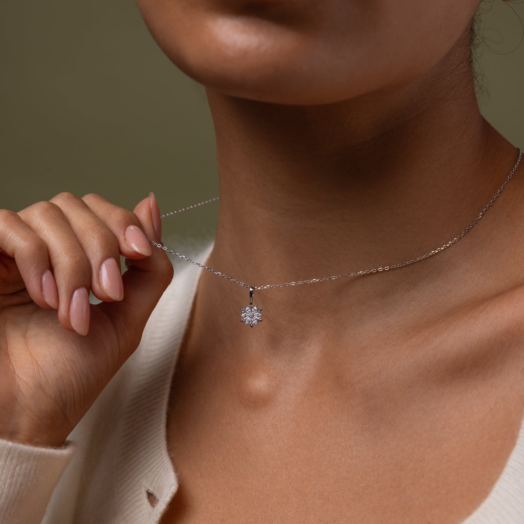 Our Diamond Poinsettia Necklace in Silver being held by a hand against a neutral background