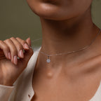 Our Diamond Poinsettia Necklace in Silver being held by a hand against a neutral background