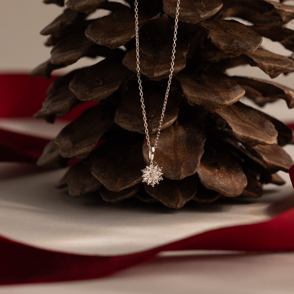 Flatlay of our Diamond Poinsettia Necklace on a pine cone with a red ribbon