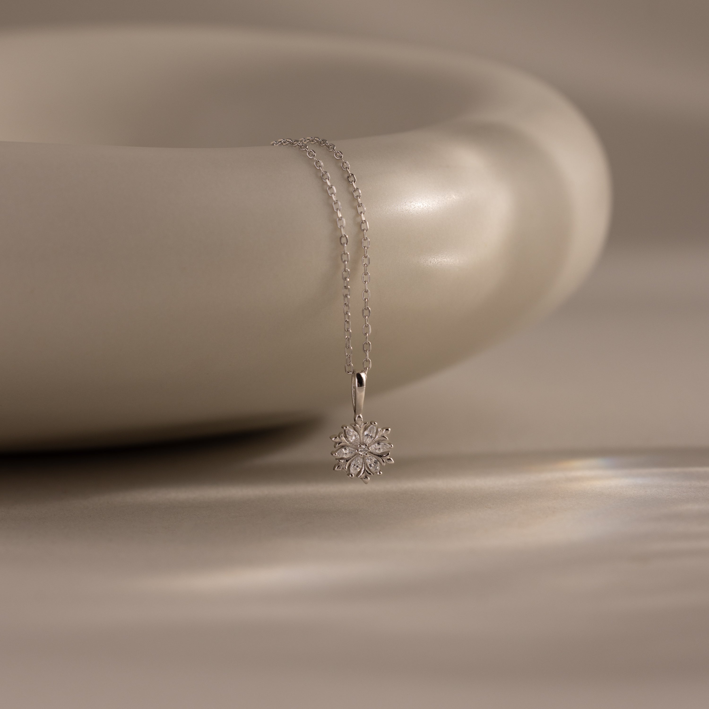 Flatlay of our Diamond Poinsettia Necklace in Silver on a beige background