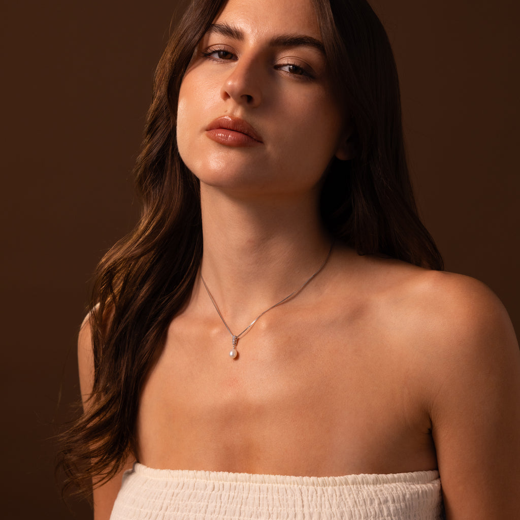 A woman with long brown hair wears a strapless white top and a Diamond Pearl Droplet Necklace in Sterling Silver against a brown background.