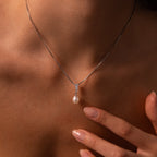 A woman touches her collarbone with manicured fingers while wearing the Diamond Pearl Droplet Necklace in Sterling Silver.