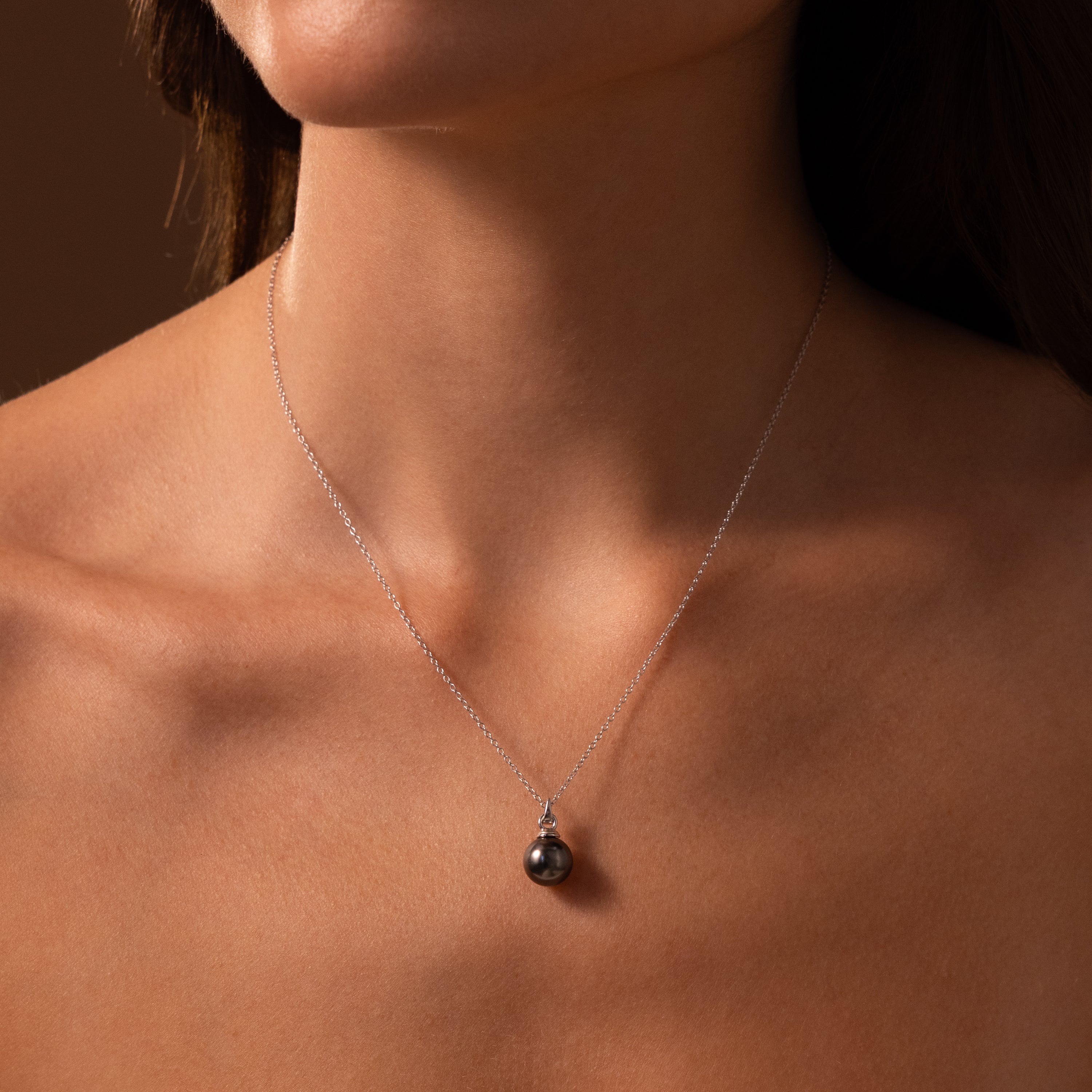 A woman wears the elegant Midnight Pearl Necklace in Sterling Silver, featuring a delicate chain and a single round black pearl pendant.