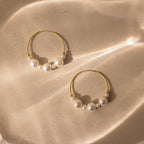 Statement Pearl Hoops featuring an open hoop design with luminous white pearls, shown on a beige surface highlighted by soft, wavy light reflections.