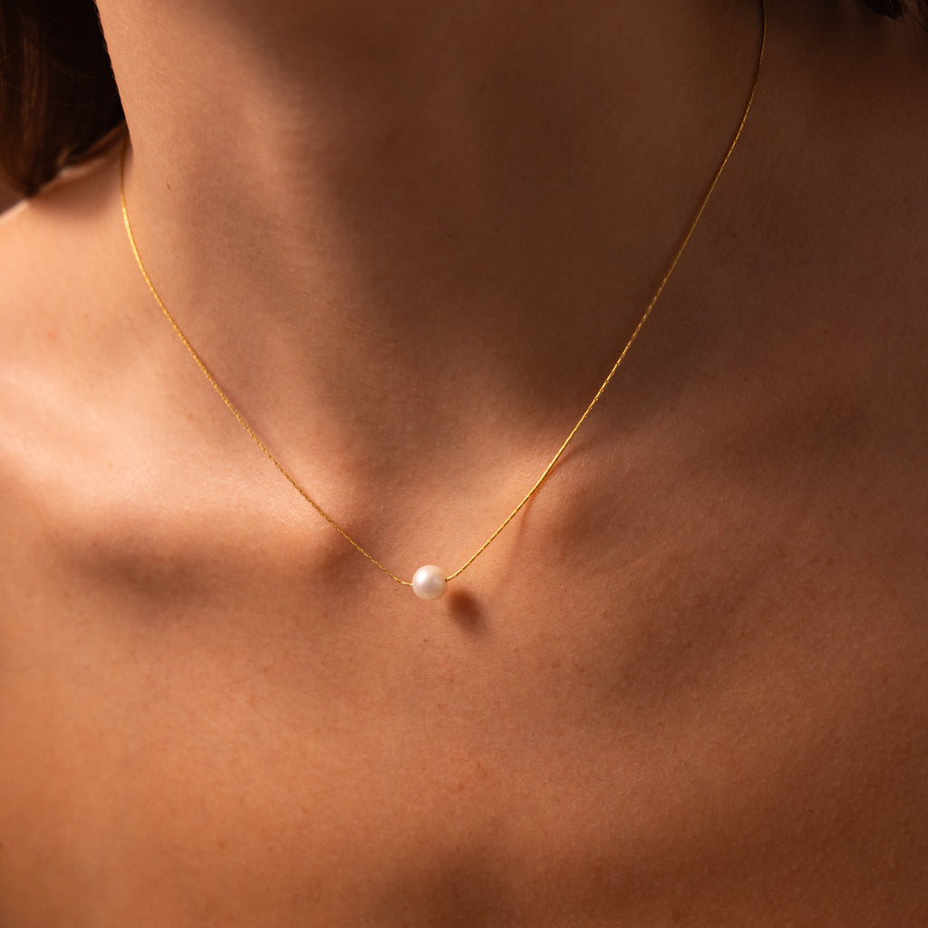 The Dainty Pearl Dot Necklace is a delicate gold layering necklace with a single pearl pendant, adding an elegant touch to any woman's look.
