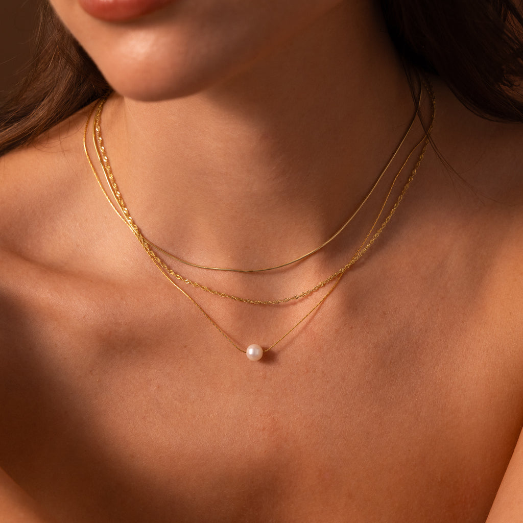 Close-up of a woman wearing layered gold necklaces, featuring the Pearl Dot Necklace with a delicate single pearl pendant, against bare skin.