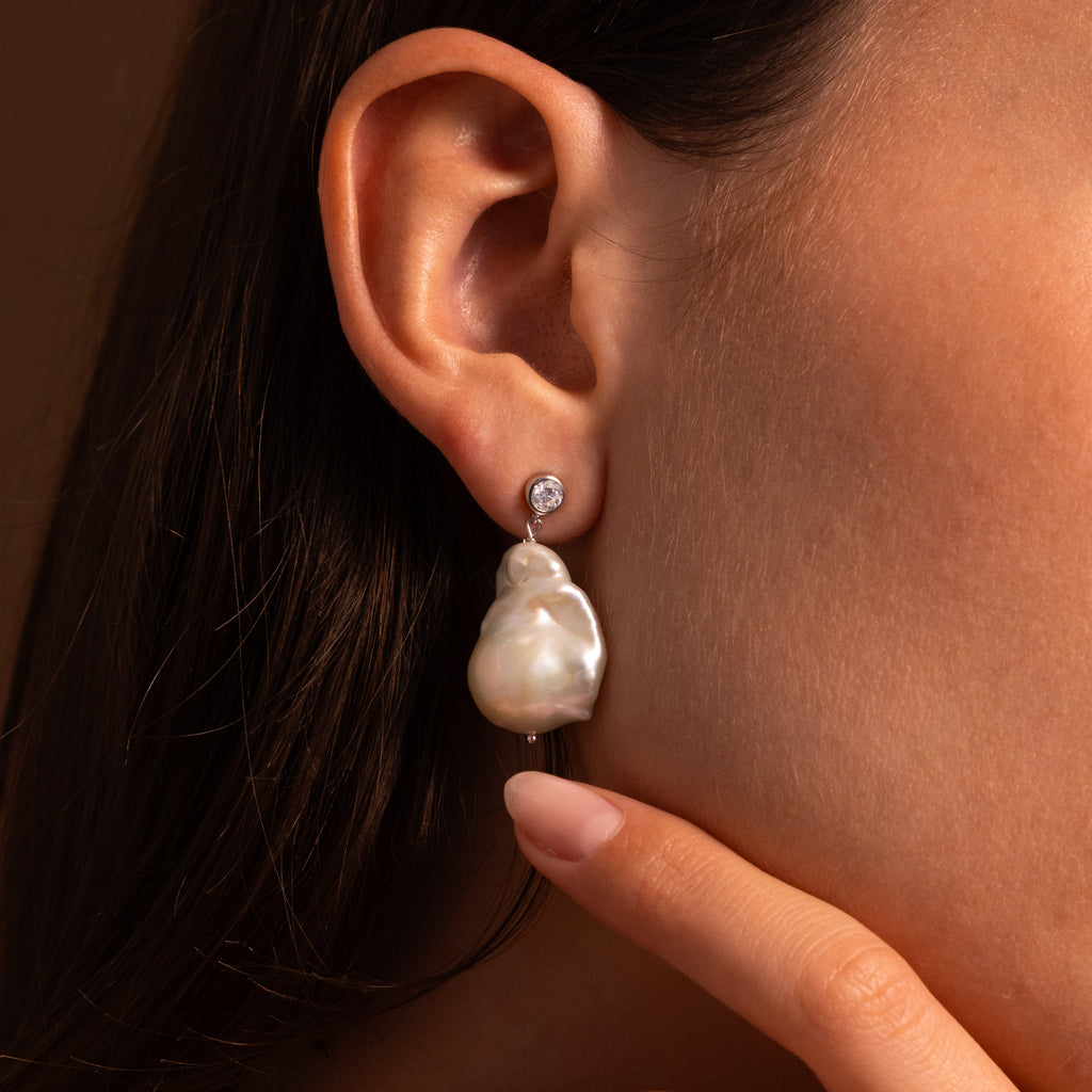 Close-up of a woman’s ear wearing Diamond Baroque Pearl Studs in Sterling Silver, featuring a baroque pearl drop with a sparkling gemstone accent above for an elegant touch.