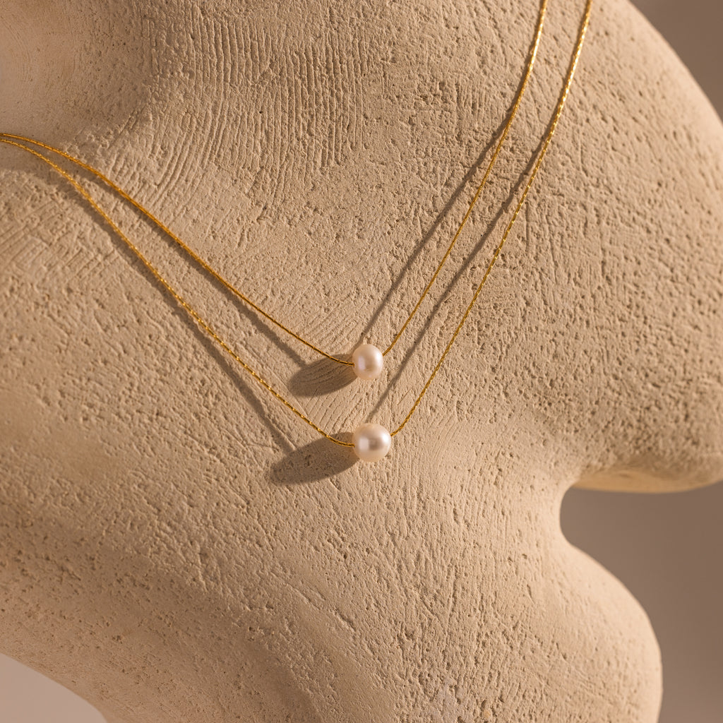 The Tiny Pearl Dot Necklace is showcased on a textured beige mannequin bust, offering an elegant accent to any delicate jewelry collection.
