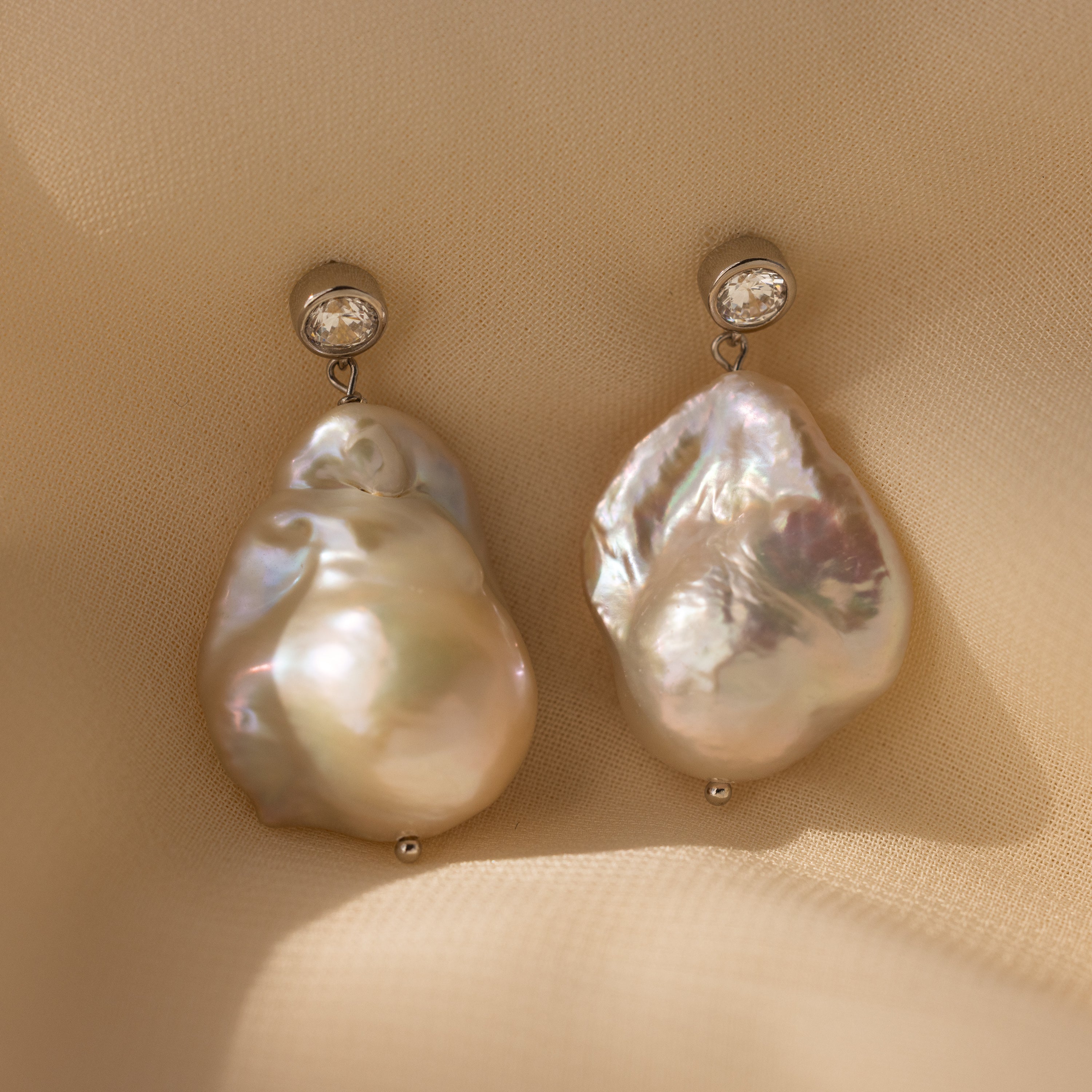 Diamond Baroque Pearl Studs in Sterling Silver showcase organic baroque pearls with diamond accents, elegantly presented on a soft beige fabric background.