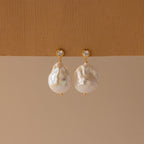 The Diamond Baroque Pearl Studs feature round white gemstones and large, irregular baroque pearls, highlighting the beauty of organic pearl jewelry in an elegant design.