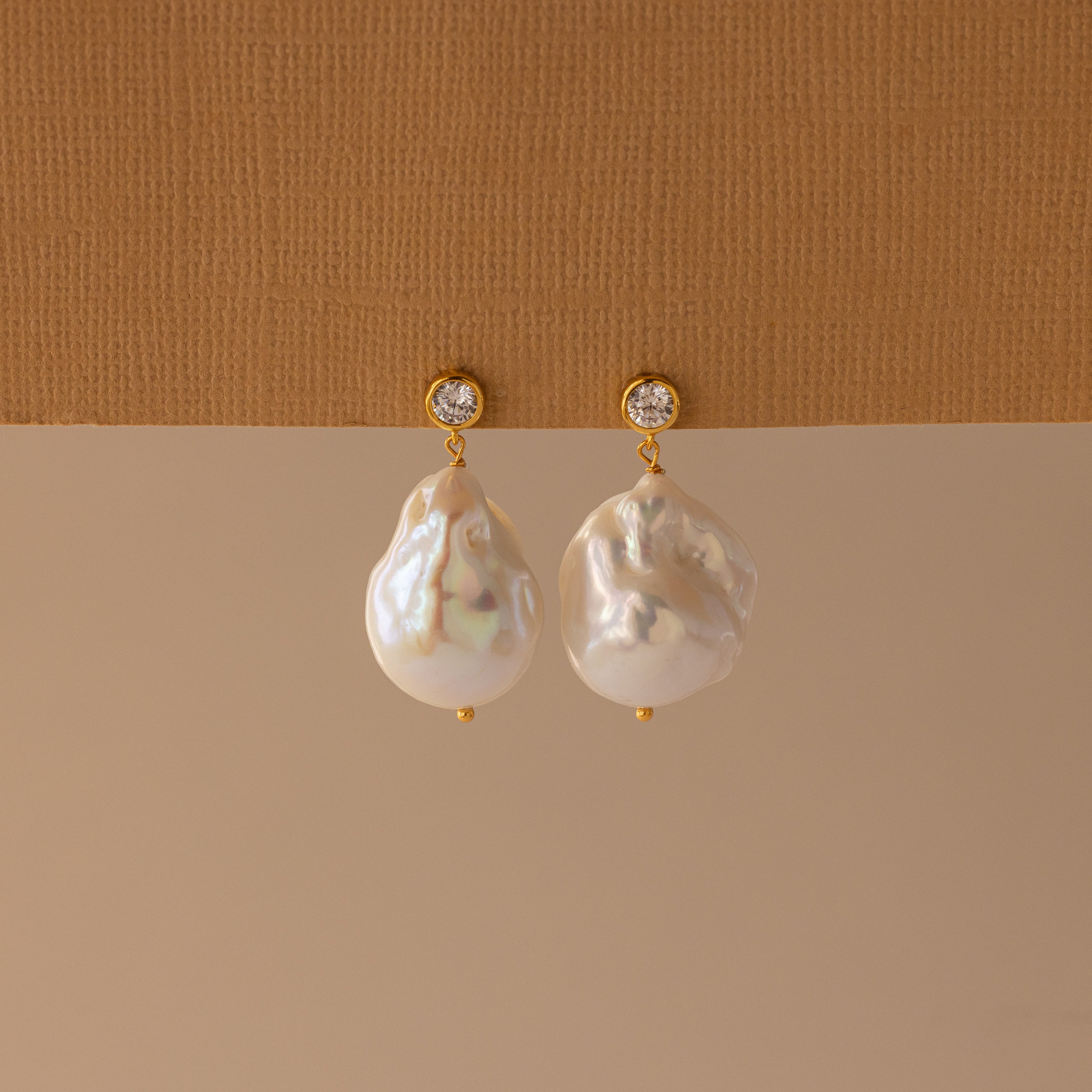 The Diamond Baroque Pearl Studs feature round white gemstones and large, irregular baroque pearls, highlighting the beauty of organic pearl jewelry in an elegant design.