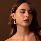 A woman with long brown hair wears Statement Pearl Hoops in Sterling Silver, gazing to the side against a brown background.