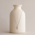 Pearl Cross Necklace in Silver showcased with luminous pearls on a textured cream vase.