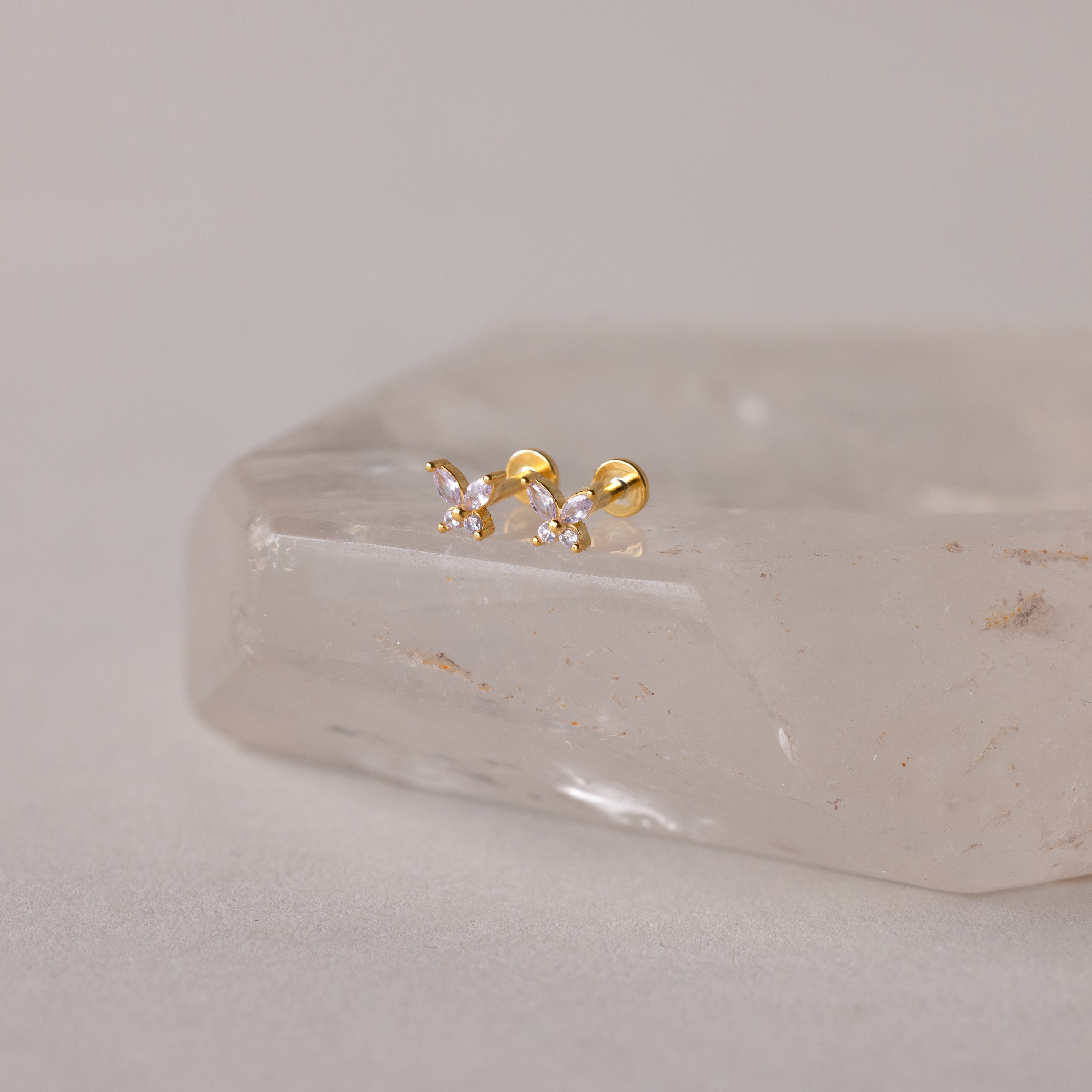 Butterfly Birthstone Flatback Studs in gold, featuring clear stones, displayed on a translucent crystal.