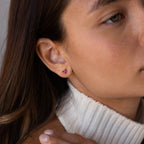 Close-up of a woman wearing Butterfly Amethyst Flatback Studs with a white turtleneck sweater.