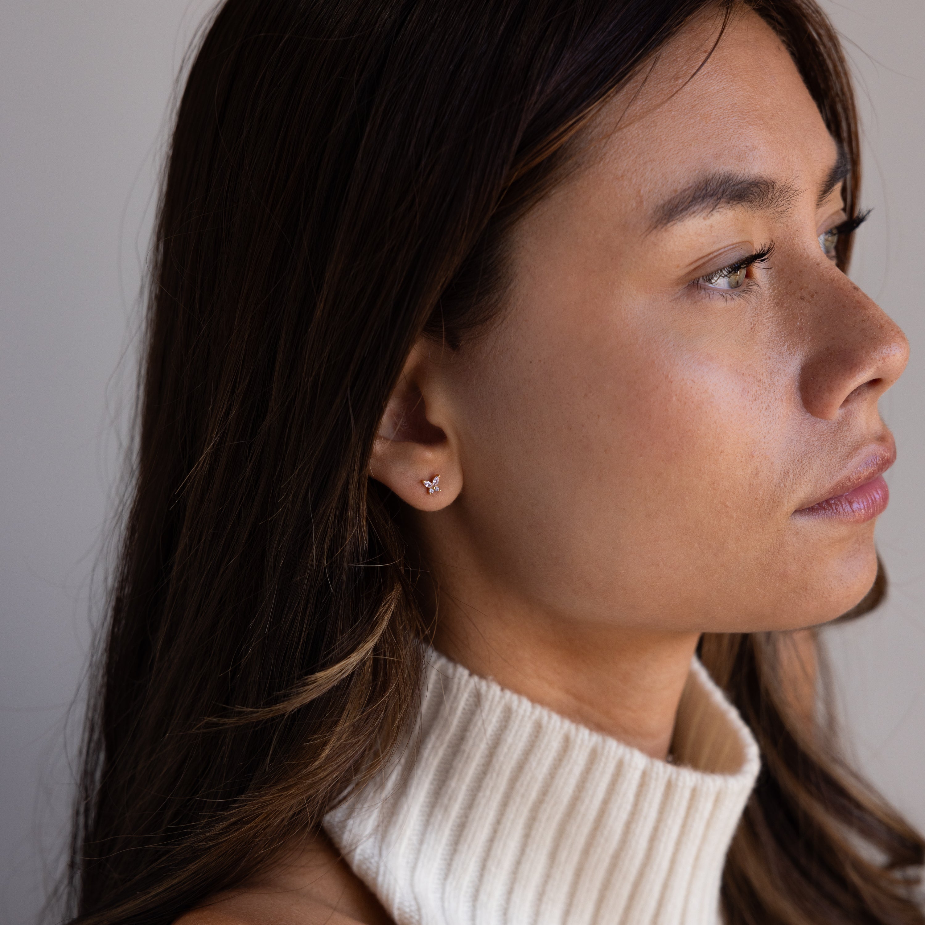 Woman with long brown hair in a cream turtleneck wears Butterfly Birthstone Flatback Studs, their subtle design adding an elegant touch as she looks to the right.