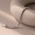 The S-Link Diamond Tennis Bracelet in White Gold is elegantly displayed on a smooth, curved beige surface in soft lighting, highlighting its timeless sophistication and classic appeal.