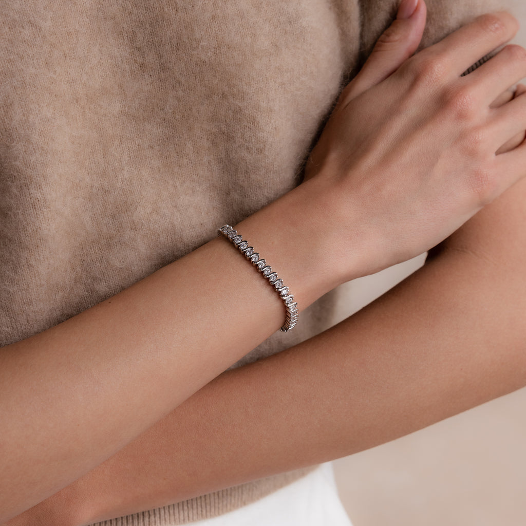 A person wearing the S-Link Diamond Tennis Bracelet in White Gold on their wrist, arms crossed over a beige sweater.